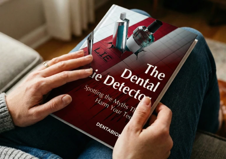 A close-up view of a person holding a red DentaBiome bonus guide book titled "The Dental Lie Detector: Spotting the Myths That Harm Your Teeth" resting on their lap.